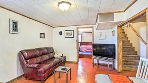 Een woonkamer met een leren bank, een bijzettafeltje, een televisie en een trap naar een andere kamer.