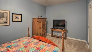 A bedroom with a bed, a dresser, a television, and framed pictures on the wall.