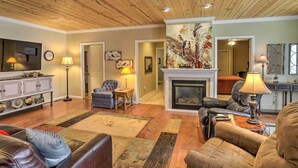 A spacious living room with a fireplace, leather sofas, a wooden ceiling, and a large painting.