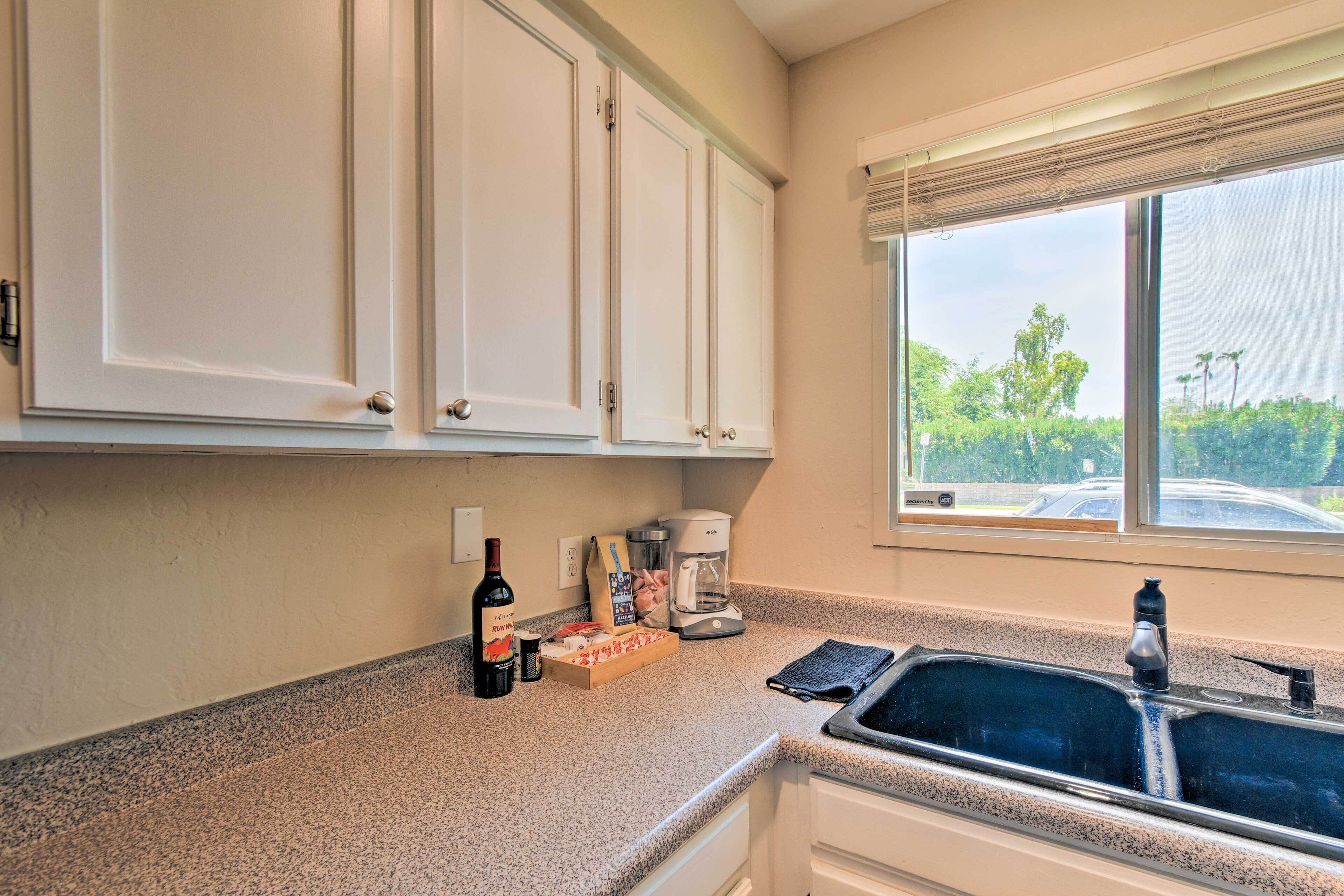 A kitchen with white cabinets, a coffee maker, a wine bottle, and a box of cereal.
