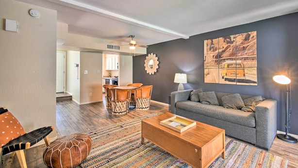 A living room with a grey sofa, wooden coffee table, patterned rug, and a dining area with wooden chairs and a table. - Scottsdale Townhome w/ Pool Access, Near Old Town! (Scottsdale)