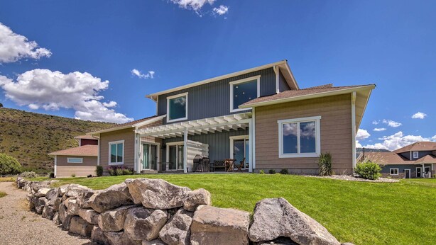A modern two-story house with a covered patio, a stone wall in the foreground, and a clear blue sky.