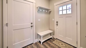 A hallway with two white doors, a bench, and a small shelf with hooks.