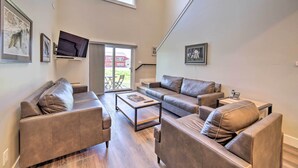 A spacious living room with a large window, a flat-screen TV mounted on the wall, and a sliding glass door leading to an outdoor area.