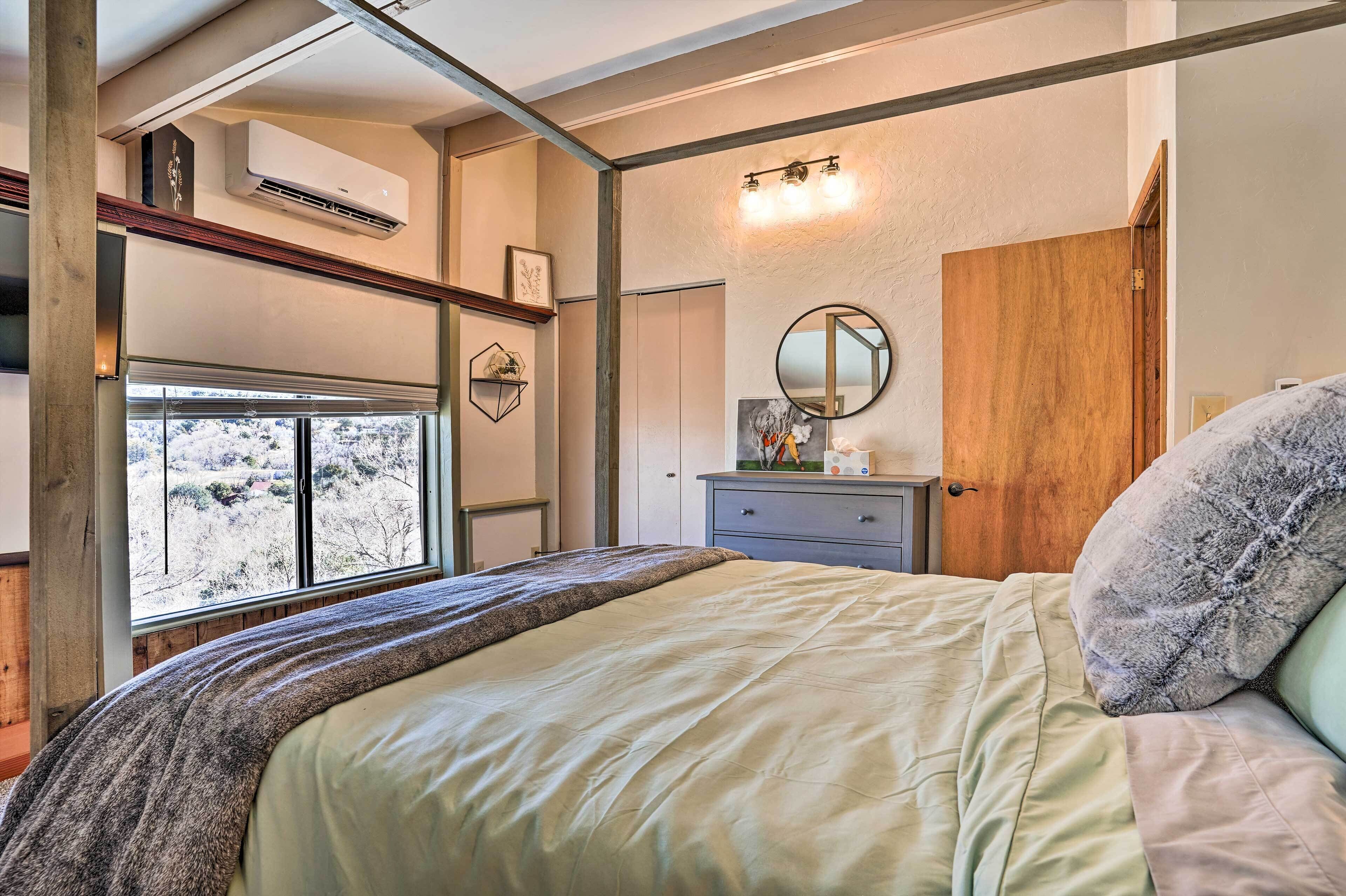 Une chambre à coucher avec un lit, une commode, un miroir et une fenêtre donnant sur des arbres.