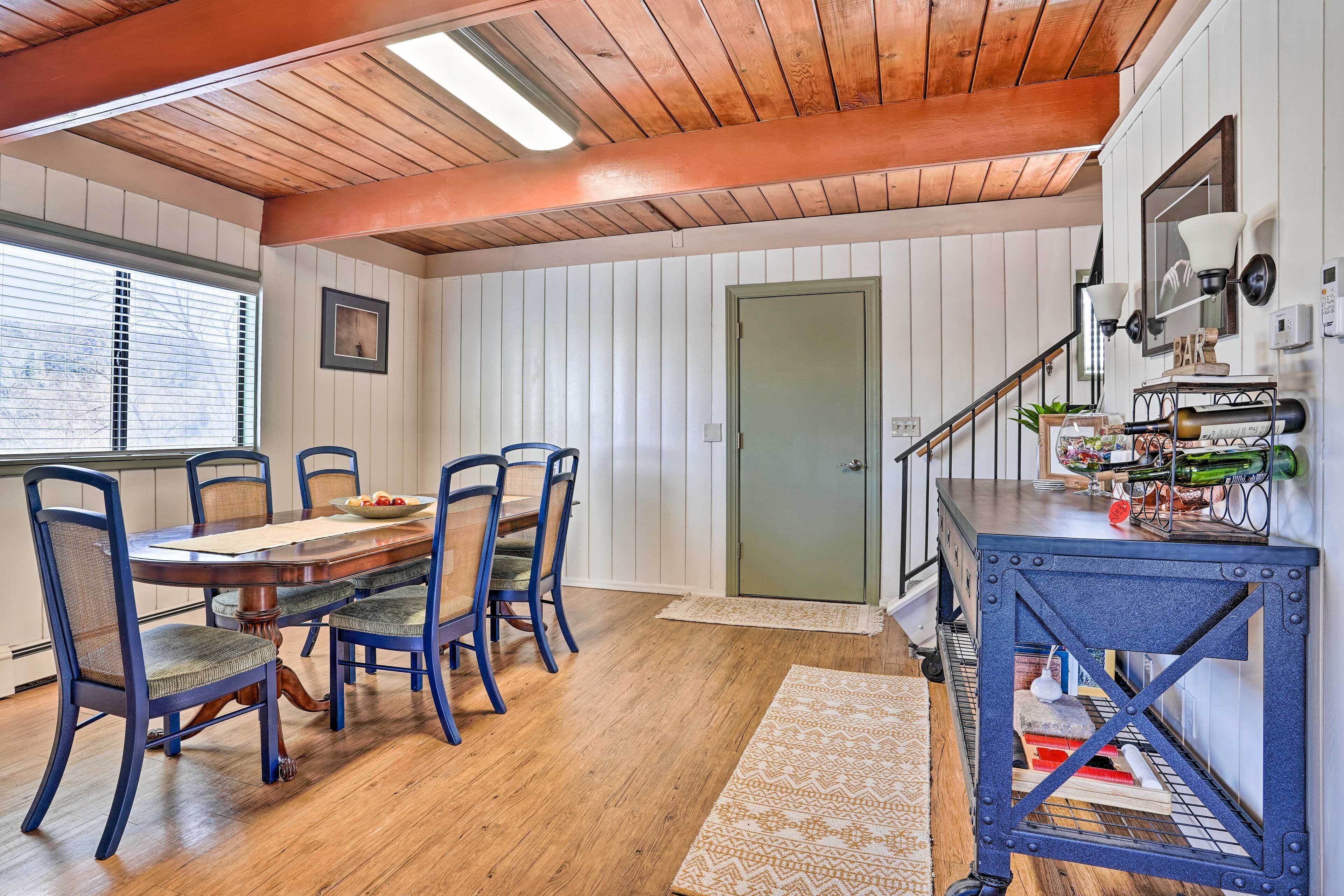 A dining area with a wooden table and blue chairs, a staircase with a metal railing, and a wall-mounted bar area.