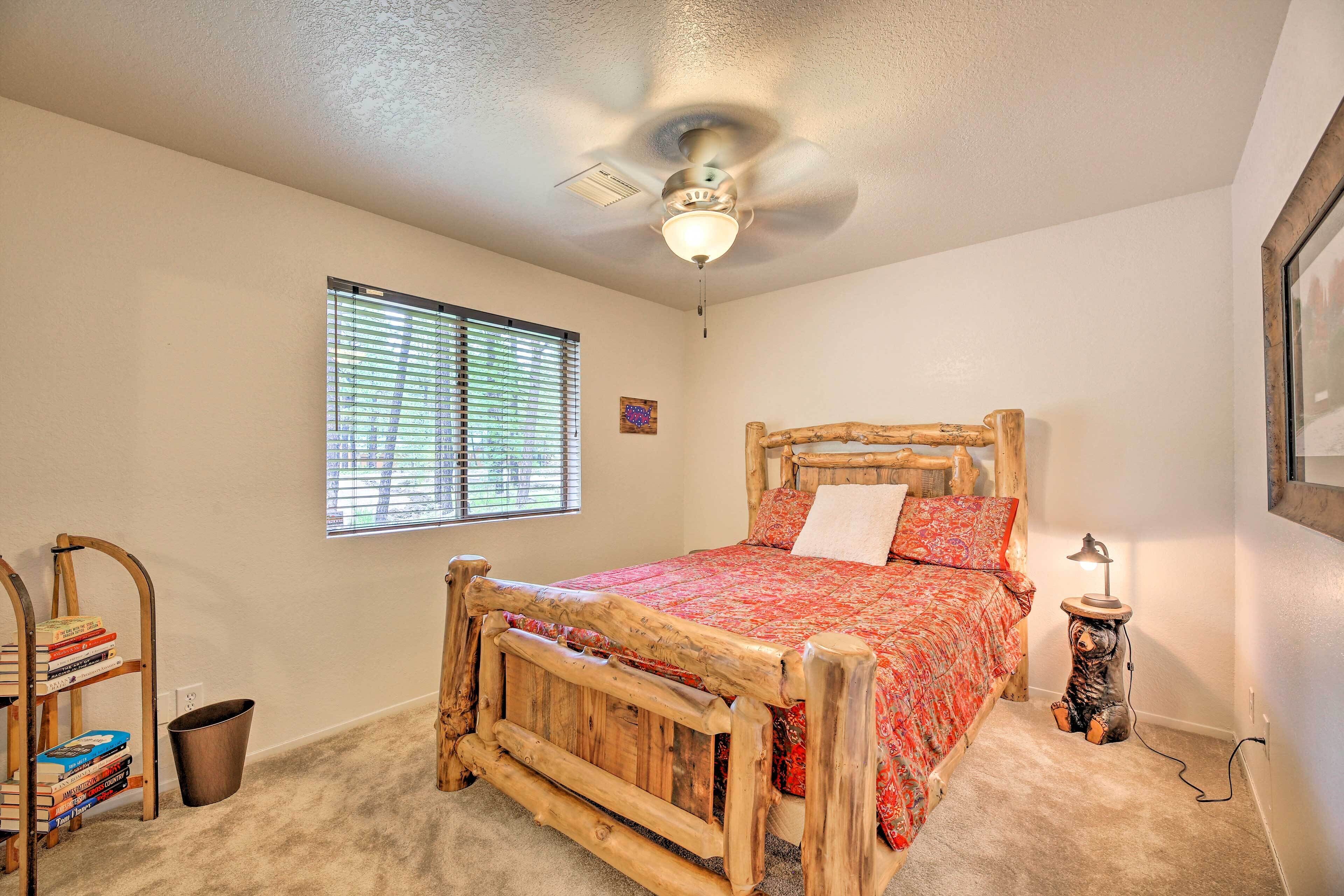 A bedroom with a wooden bed, a ceiling fan, a window with blinds, a bookshelf, and a nightstand with a lamp.