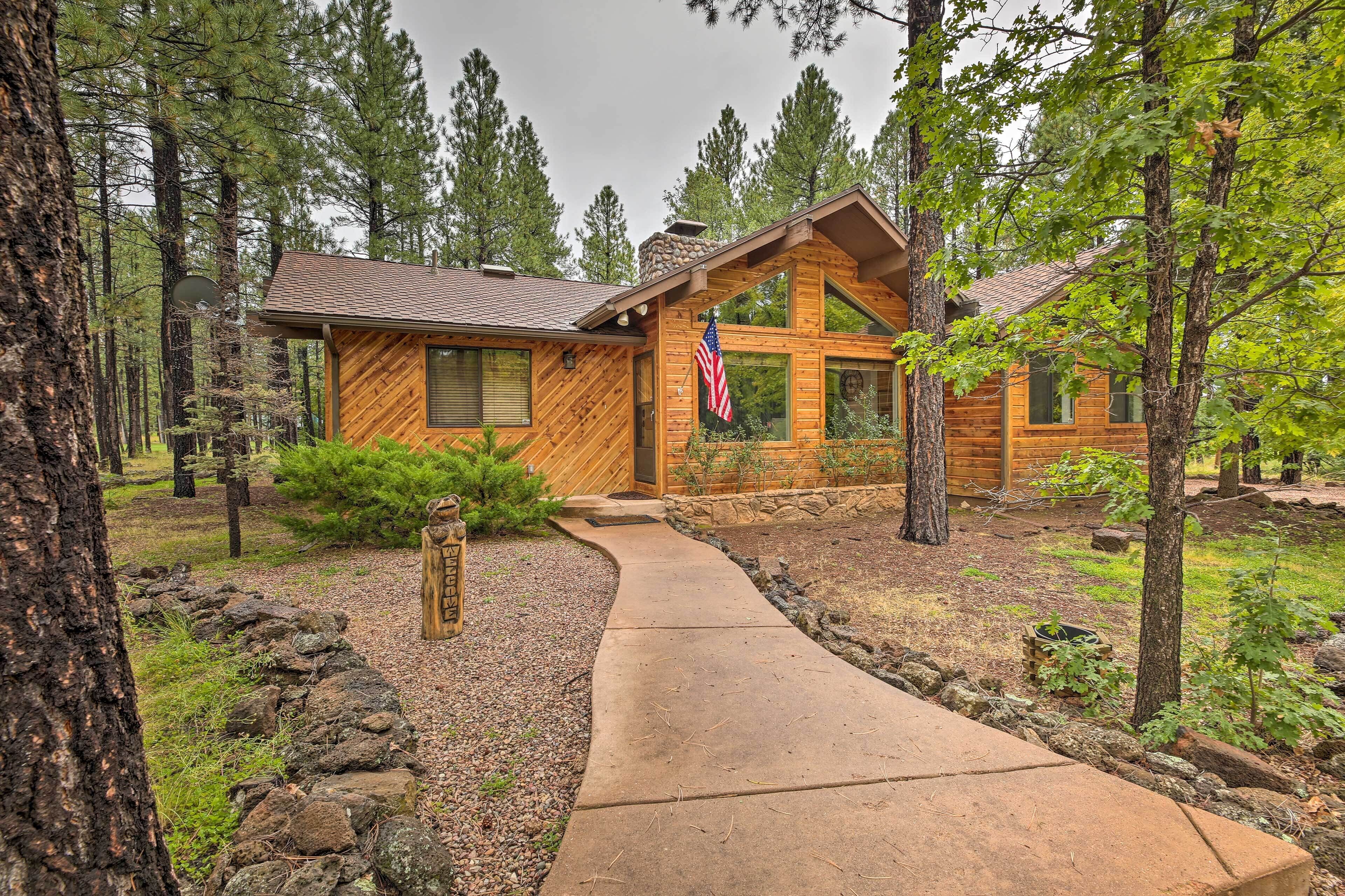 A wooden cabin with a stone pathway leading to the entrance, surrounded by trees.