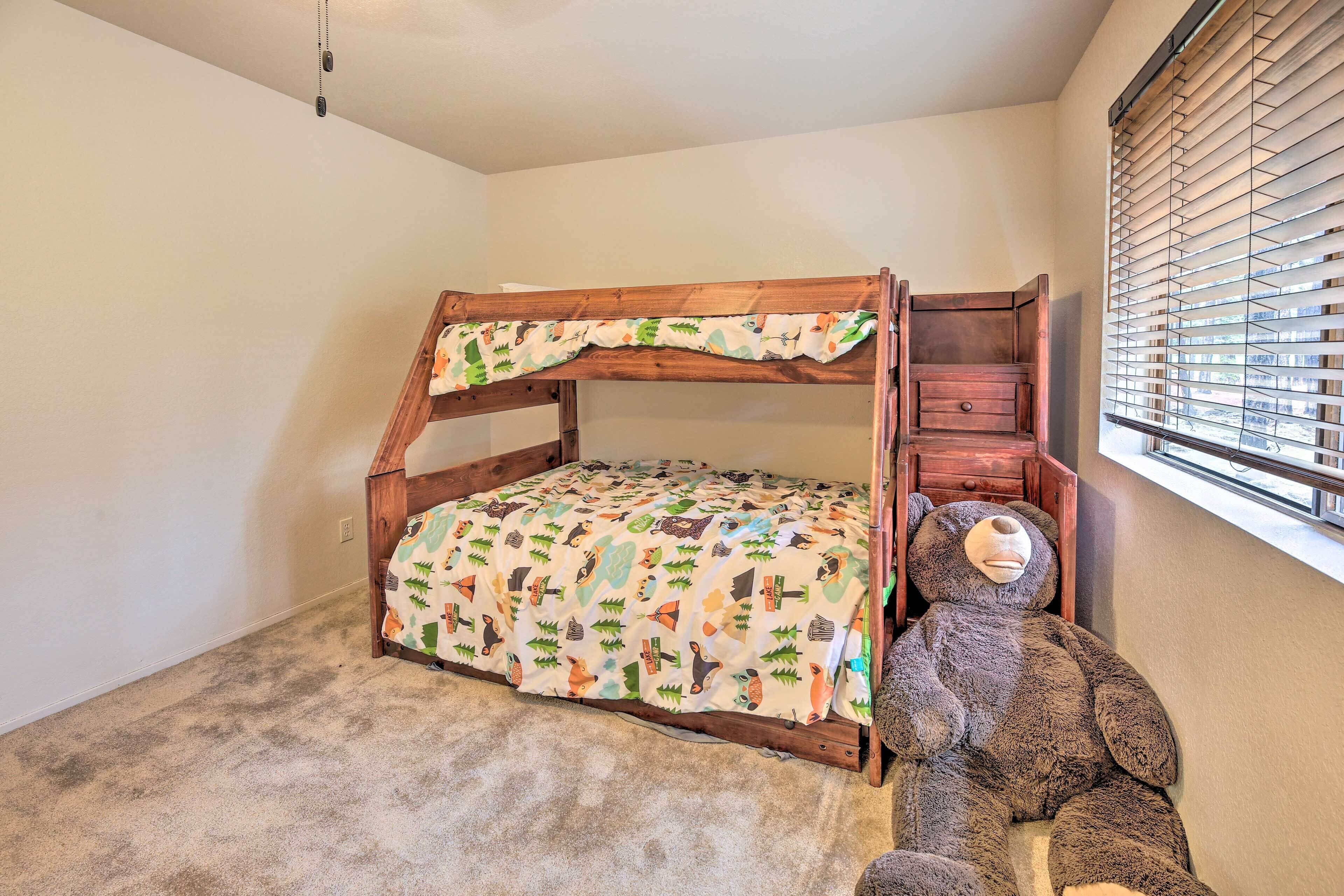 A bunk bed with a patterned bedspread, a wooden headboard, and a large teddy bear beside it.