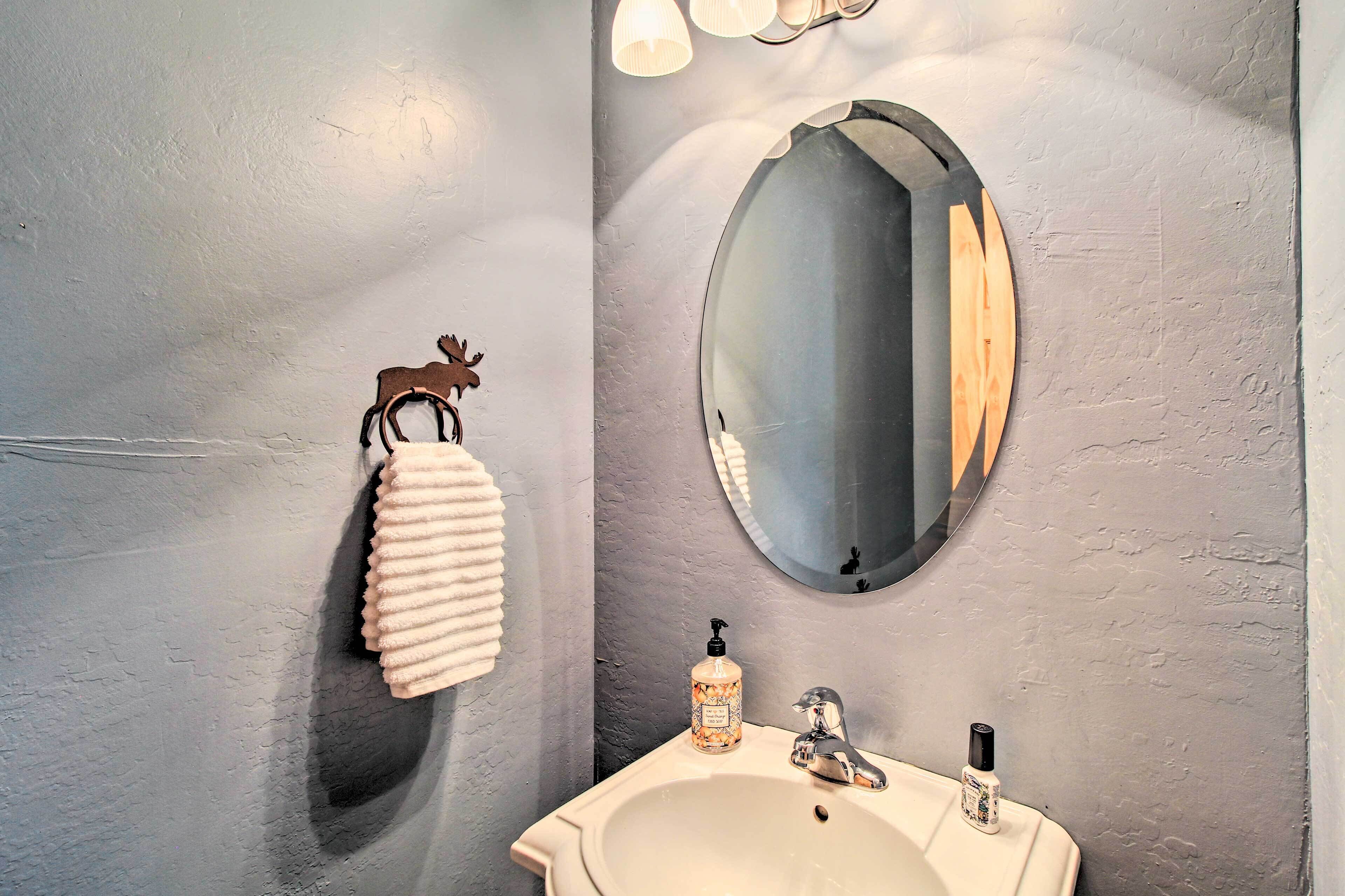 A bathroom with a white sink, a round mirror, and a towel rack with a towel.