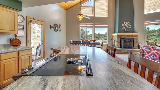 A spacious kitchen with a large island, wooden cabinets, and a stone fireplace. - Secluded Show Low Home Near Hiking Trails! (Show Low)