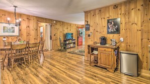 Ein Zimmer mit Holzwänden, einem Esstisch, Stühlen, einem Kühlschrank und einem Fernseher.