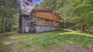 Eine Holzhütte mit Veranda, umgeben von Bäumen und einem grünen Rasen.