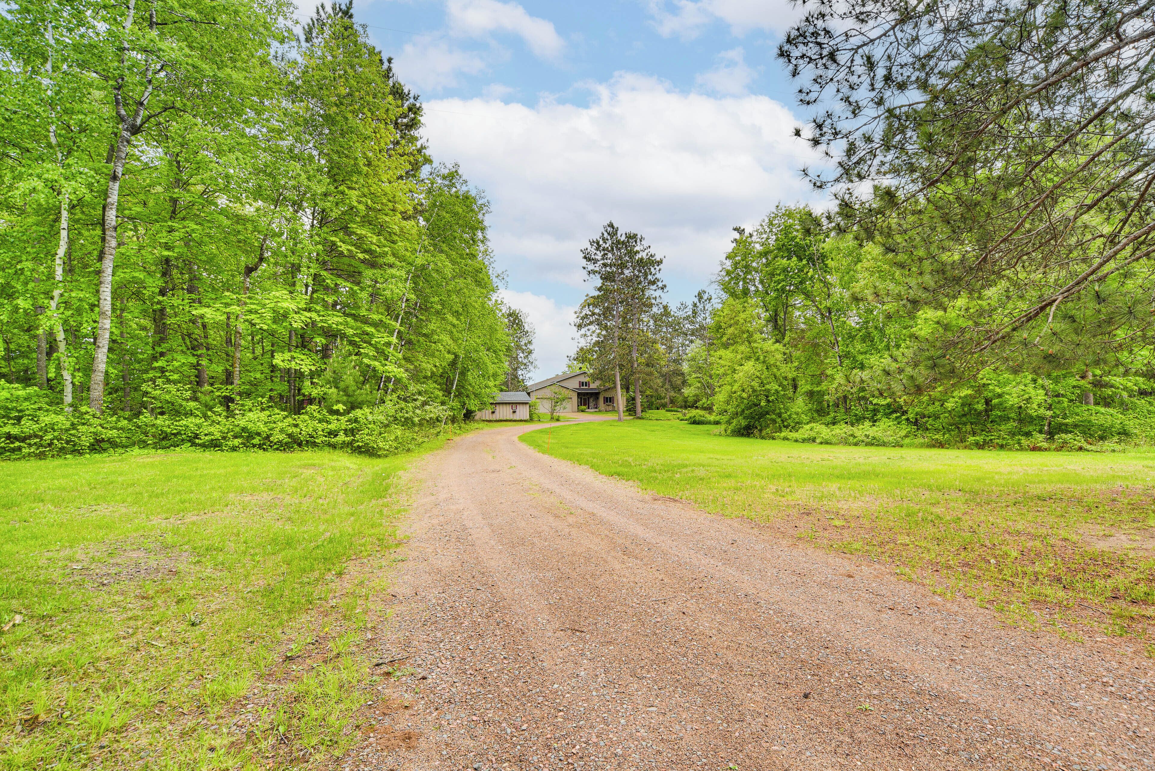 A gravel road leading to a house surrounded by dense green trees.