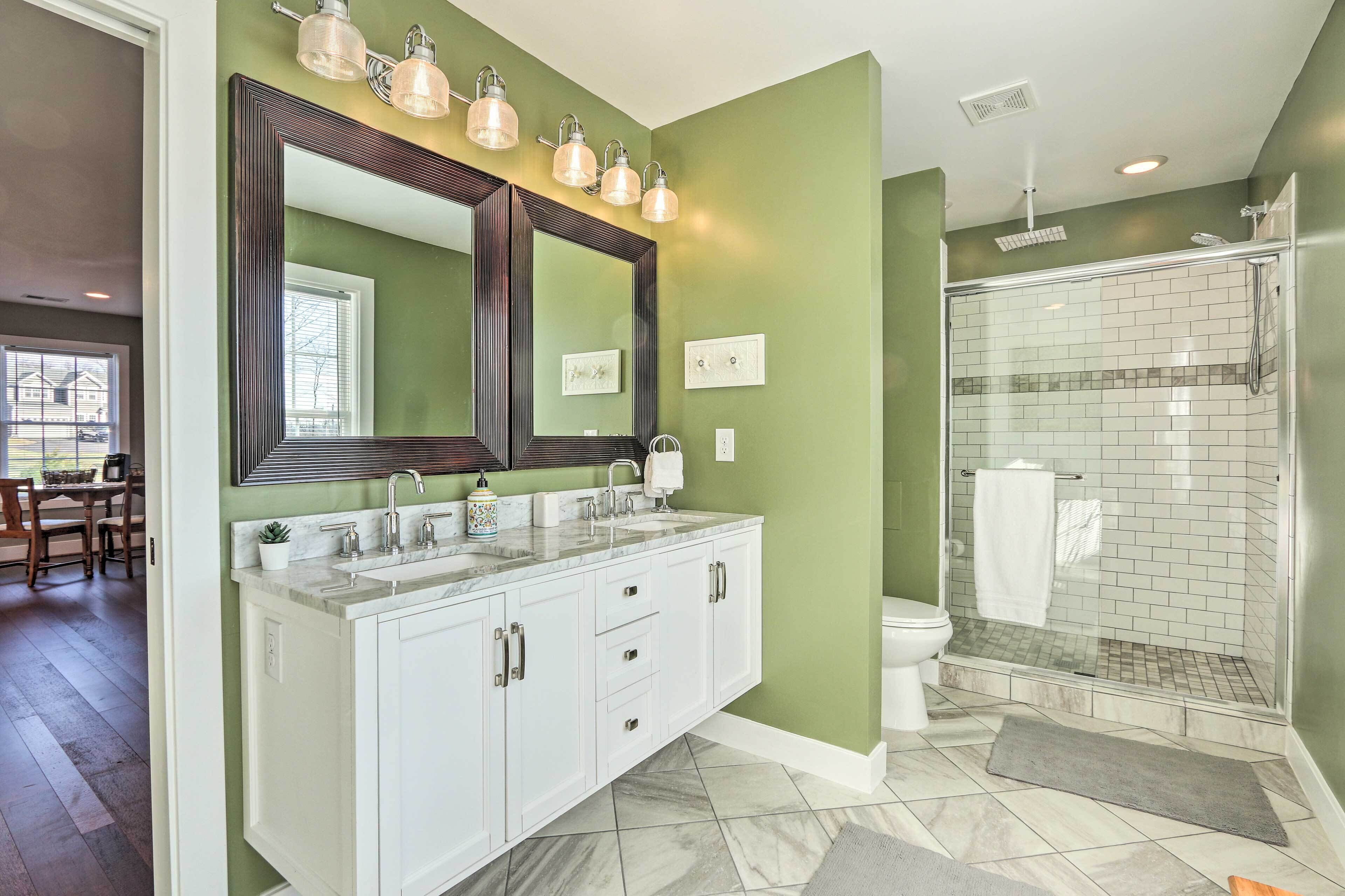 Une salle de bain avec un grand miroir, deux lavabos, une douche et un sol carrelé.