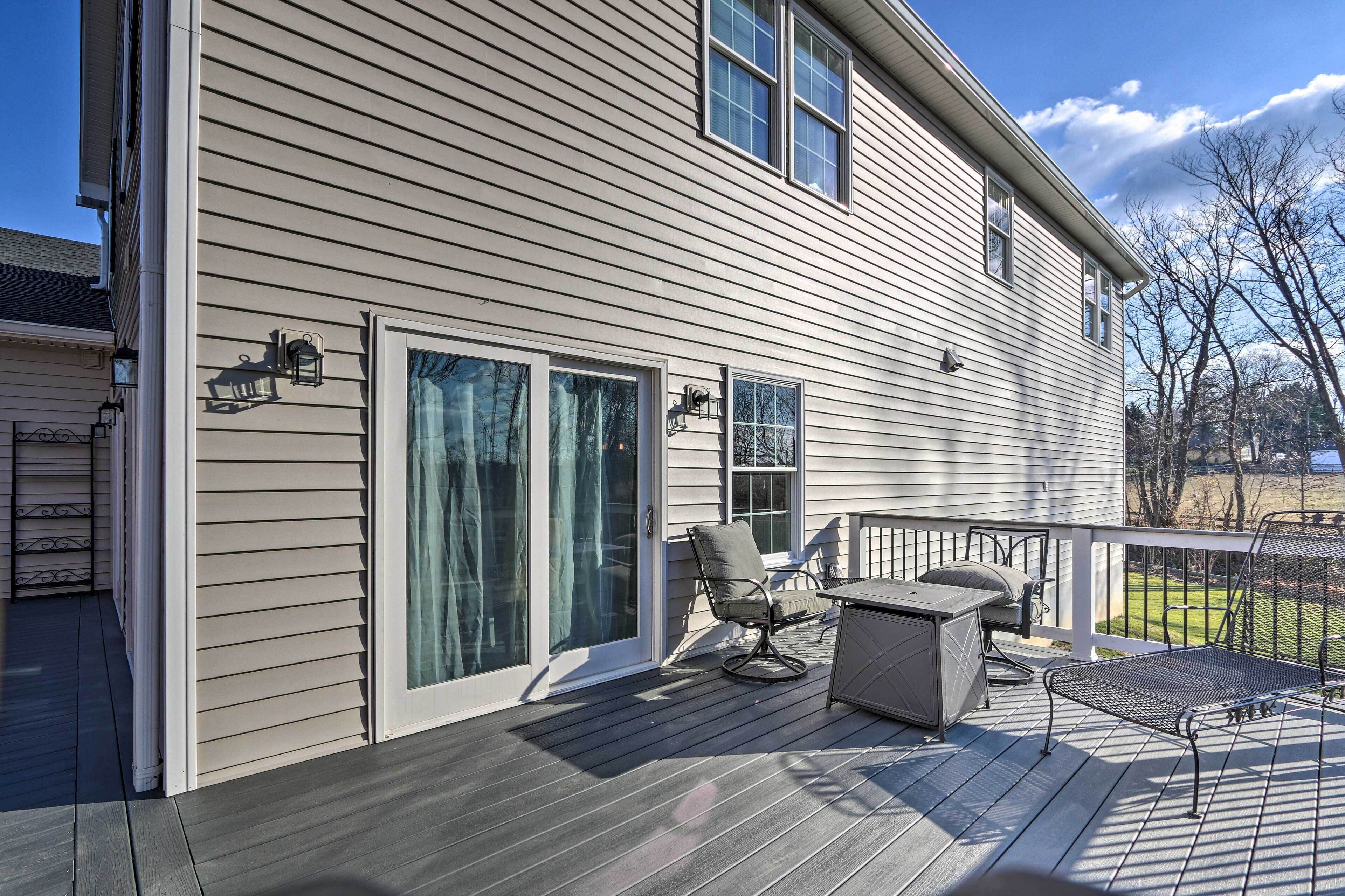 A covered deck with outdoor furniture, large sliding glass doors, and a view of the surrounding landscape.