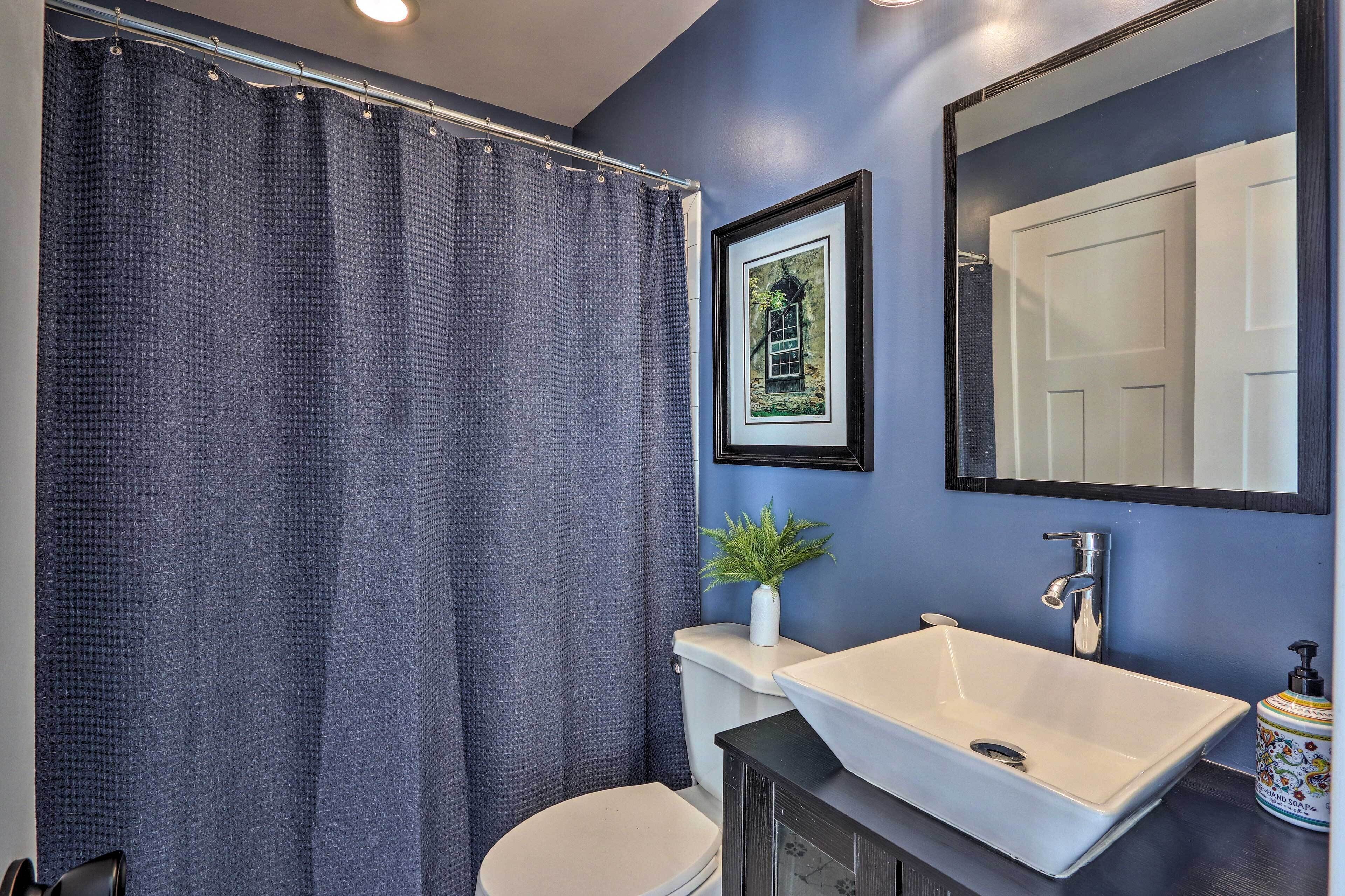 A bathroom with a white sink, a toilet, a shower curtain, a framed picture on the wall, and a mirror.