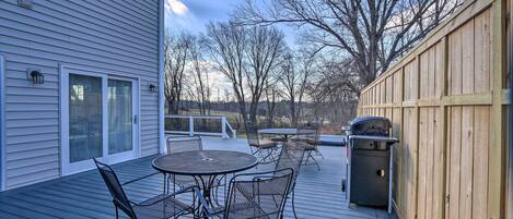 A wooden deck with outdoor furniture, a barbecue grill, and a view of trees and a house in the background.