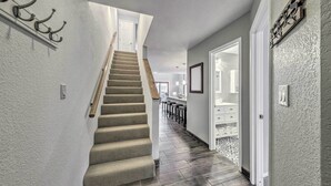 A hallway with a carpeted staircase, a white door, and a wall-mounted light fixture. - Dreamy, Family-friendly Cloudcroft Townhome! (Cloudcroft)