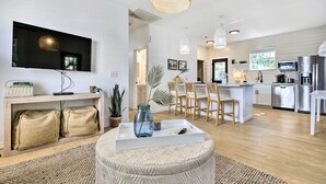 Een moderne woonkamer met een flatscreen televisie, een houten console en een eethoek met stoelen.