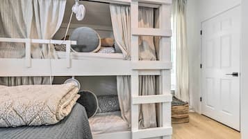 A bunk bed room with a white door, a small window with curtains, and a rug on the floor.