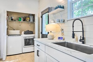 A modern kitchen with white cabinetry, a built-in oven, a dishwasher, and a large window providing natural light. - Modern & Chic Gulfport Escape: Walk to Beach! (Gulfport)