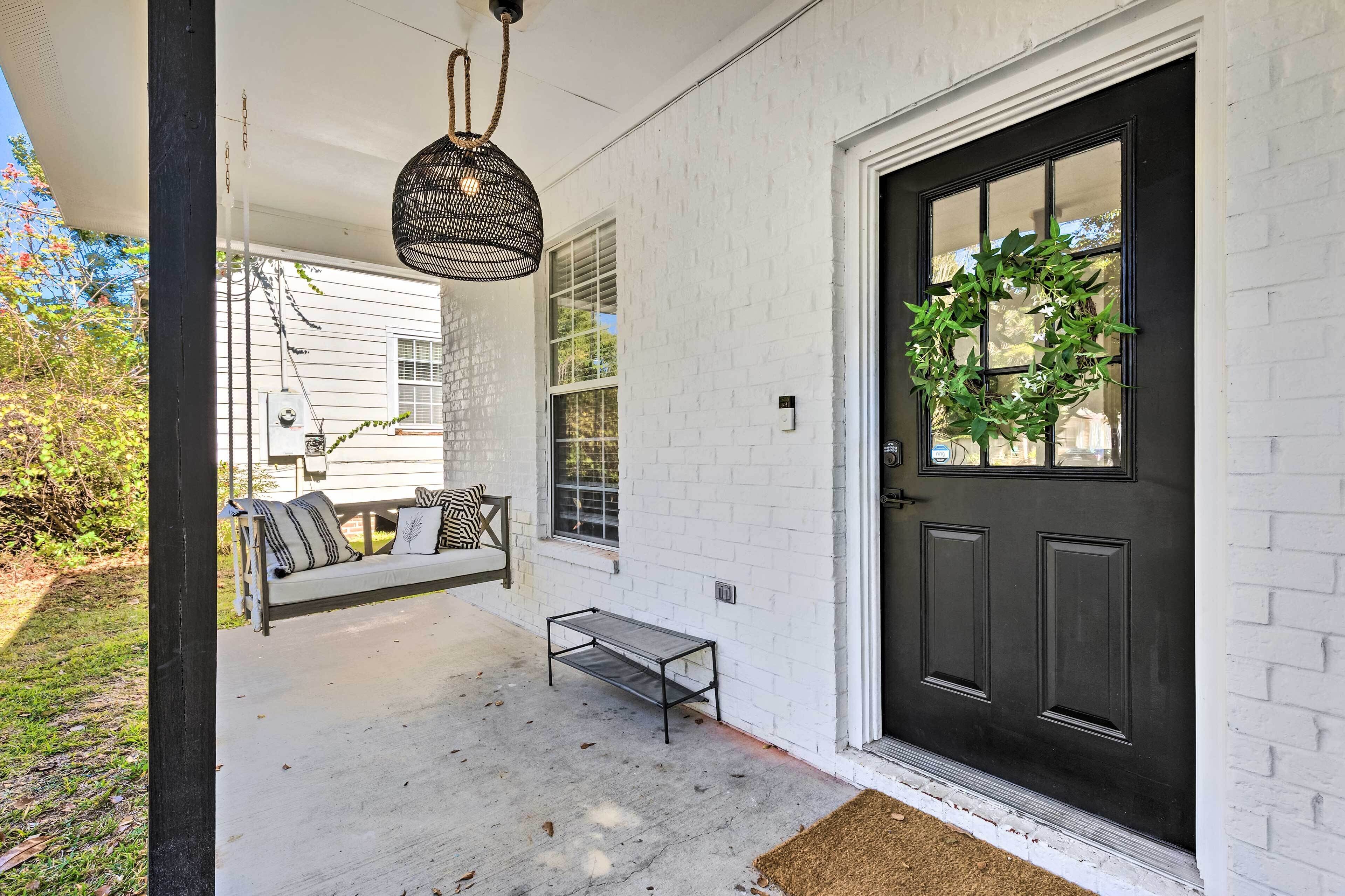 A porch with a bench, a hanging light fixture, and a black door with a wreath.