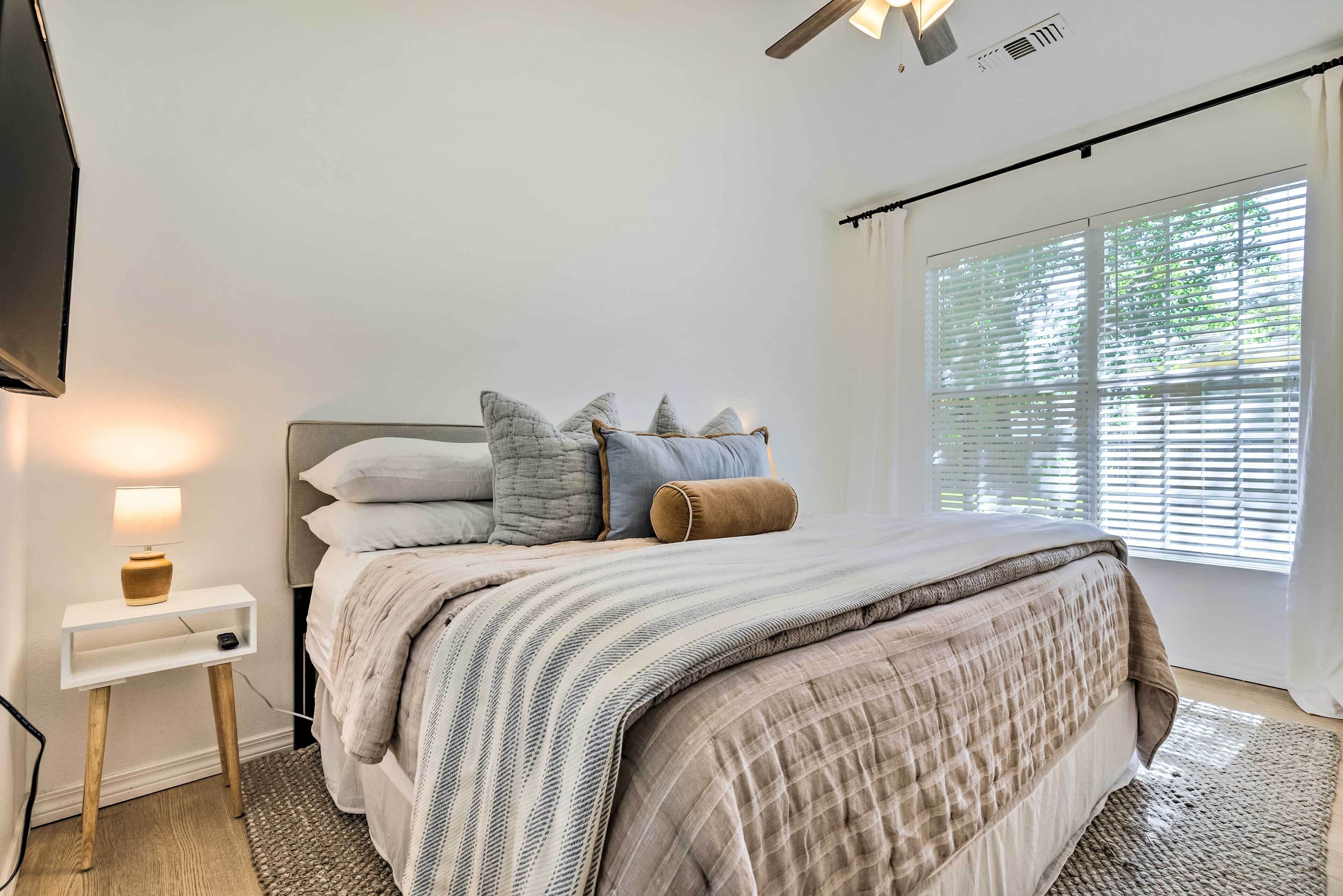 A bedroom with a bed, bedside table, lamp, and window with blinds.