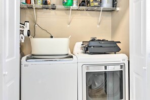 Un espace buanderie compact comprenant un lave-linge, un sèche-linge et une étagère au-dessus pour ranger les produits de nettoyage.