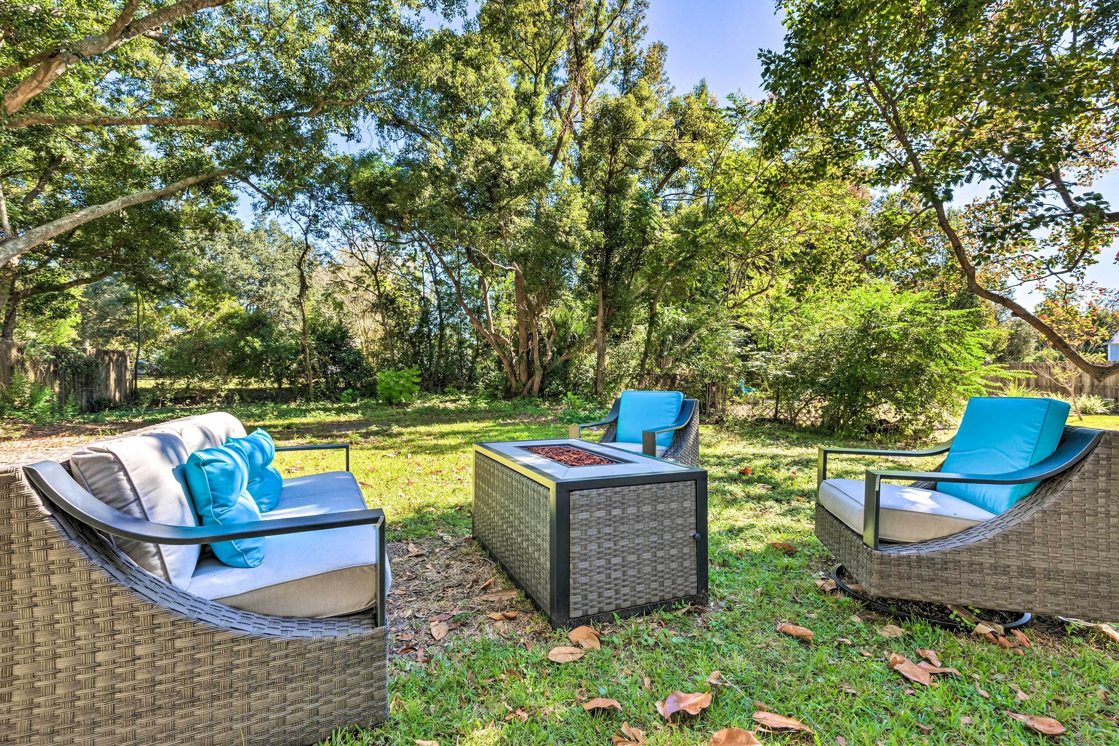 An outdoor seating area with wicker furniture and cushions, surrounded by trees.