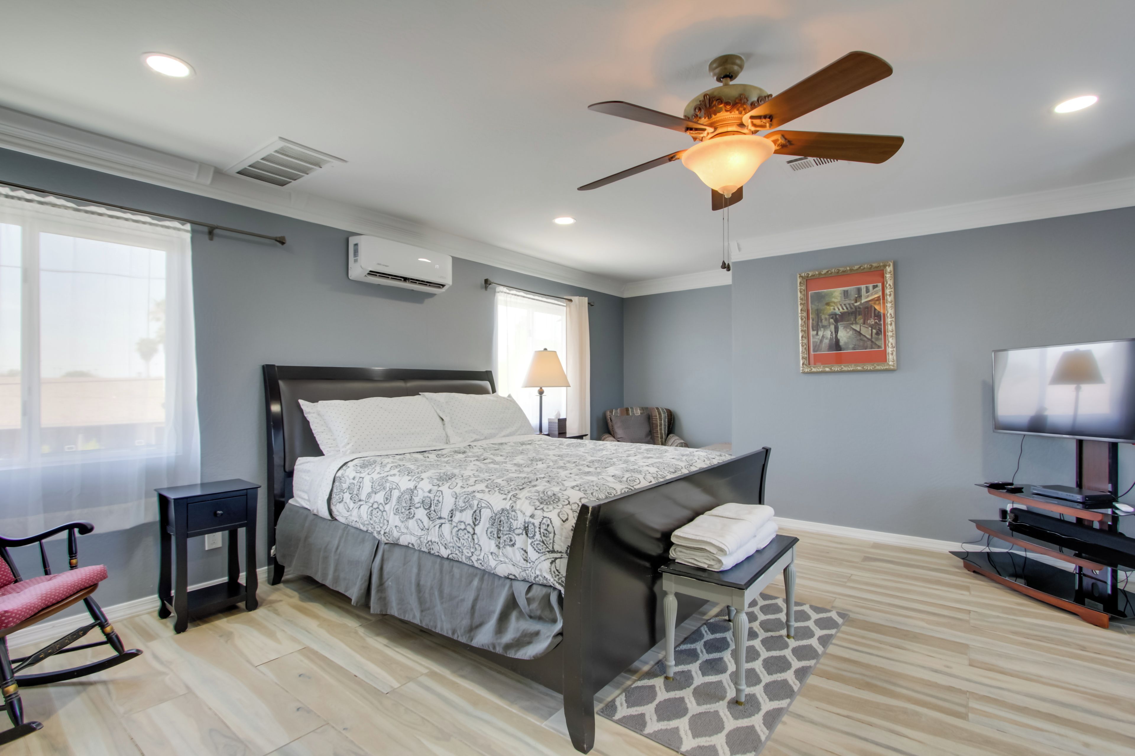 A modern bedroom with a large bed, a ceiling fan, a TV, and a window with curtains.
