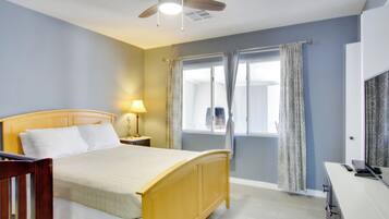 A bedroom with a wooden bed, a nightstand, a lamp, a ceiling fan, a window with curtains, and a TV on a dresser.