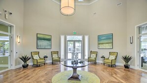 A spacious lobby with a round table at the center, flanked by four green armchairs, a large window with a view, and two paintings on the walls. - Sunny Ft Myers Abode w/ Community Amenities! (Fort Myers)