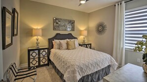 A bedroom with a bed, two bedside tables with lamps, a ceiling fan, a wall art piece, a decorative mirror, and a window with blinds. - Sunny Ft Myers Abode w/ Community Amenities! (Fort Myers)