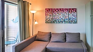 A grey sectional sofa with two cushions, a floor lamp, and a colorful abstract painting on the wall. - Surfside 'sandcastle Suite' w/ Balcony & 2 Pools! (Corpus Christi)
