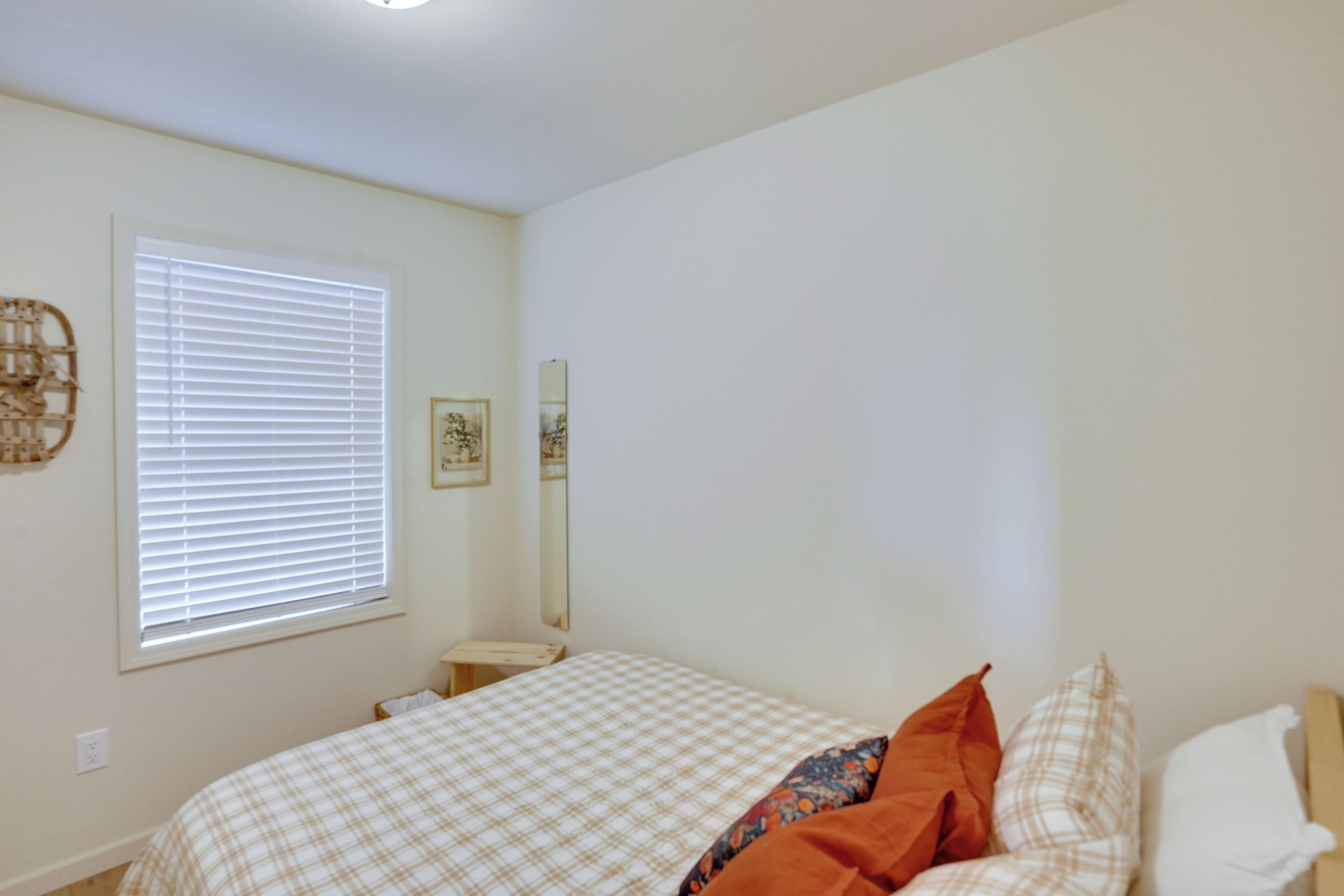 Un dormitorio con cama, ventana con persianas, mesita de noche y espejo adosado a la pared.