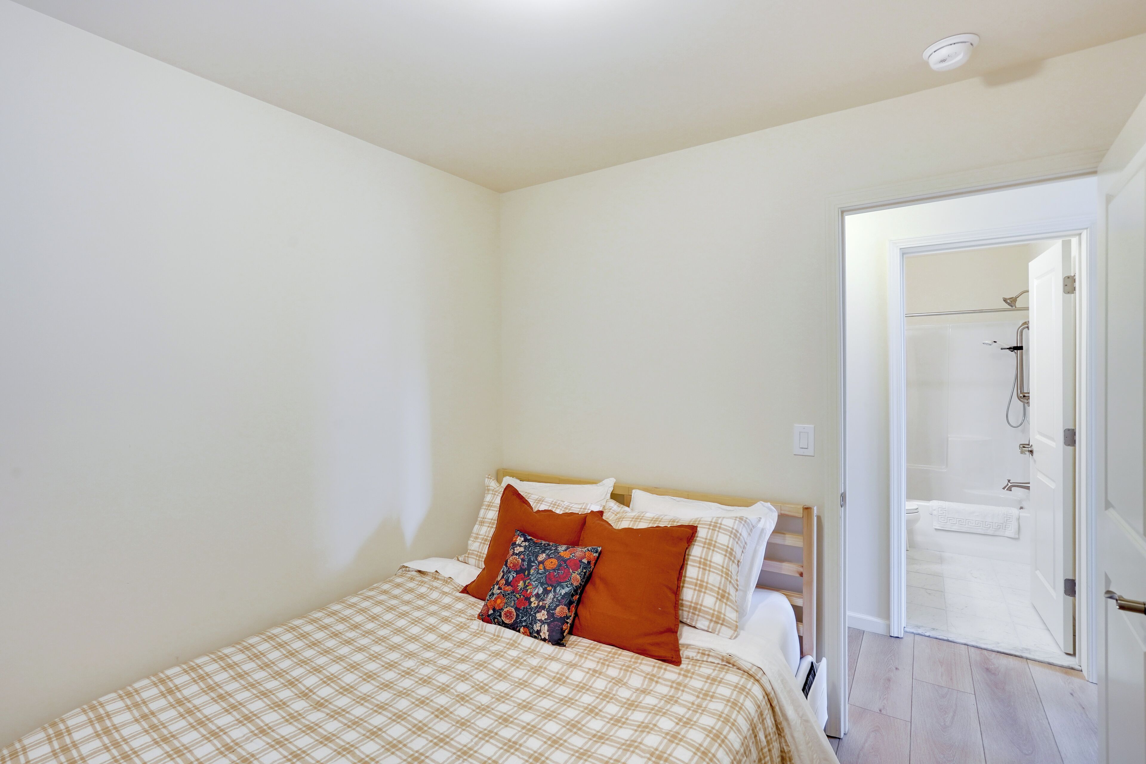 A bedroom with a bed, a door leading to a bathroom, and a visible shower area.