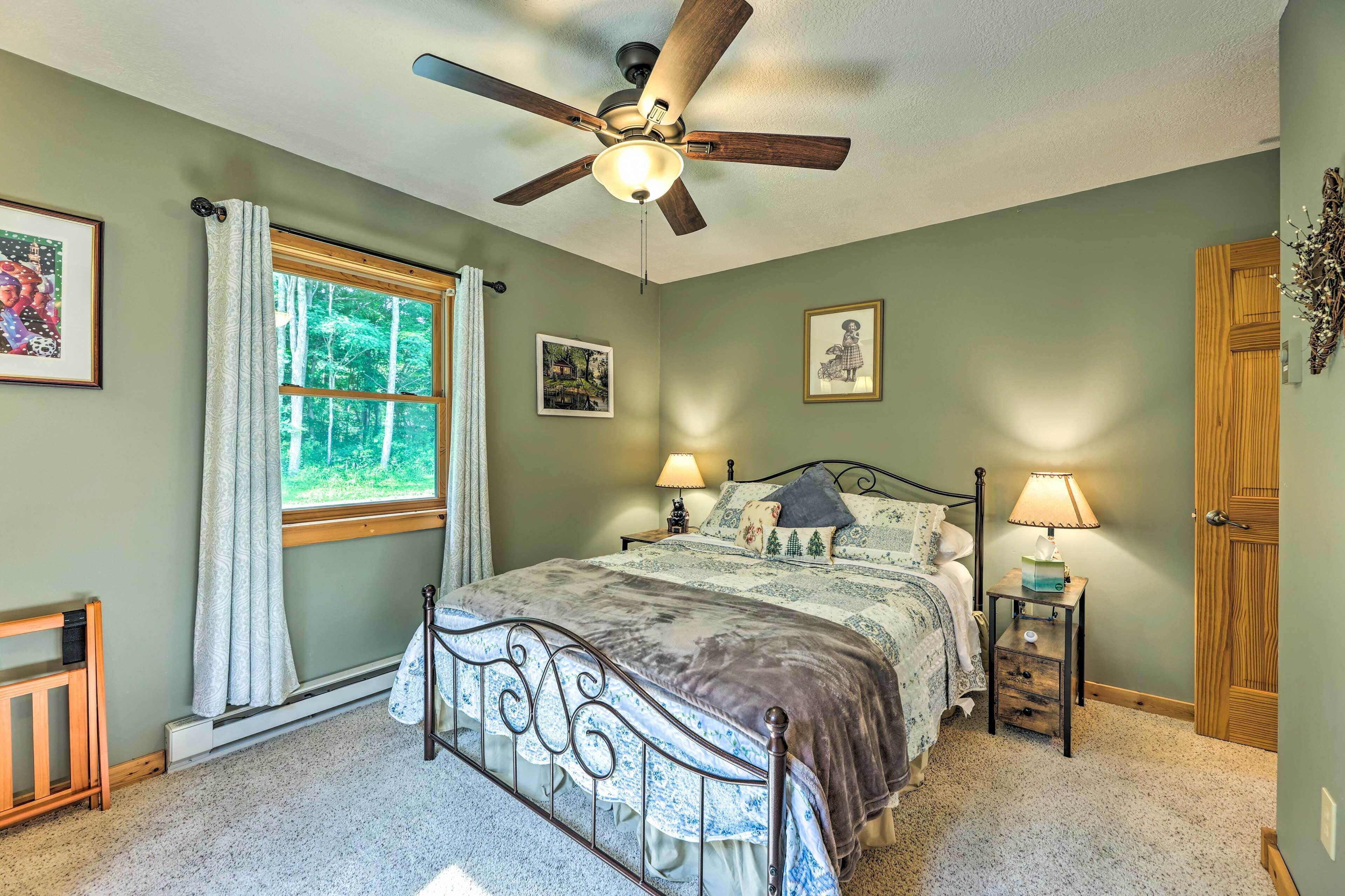 A bedroom with a bed, two bedside tables with lamps, a ceiling fan, a window with curtains, and a door.