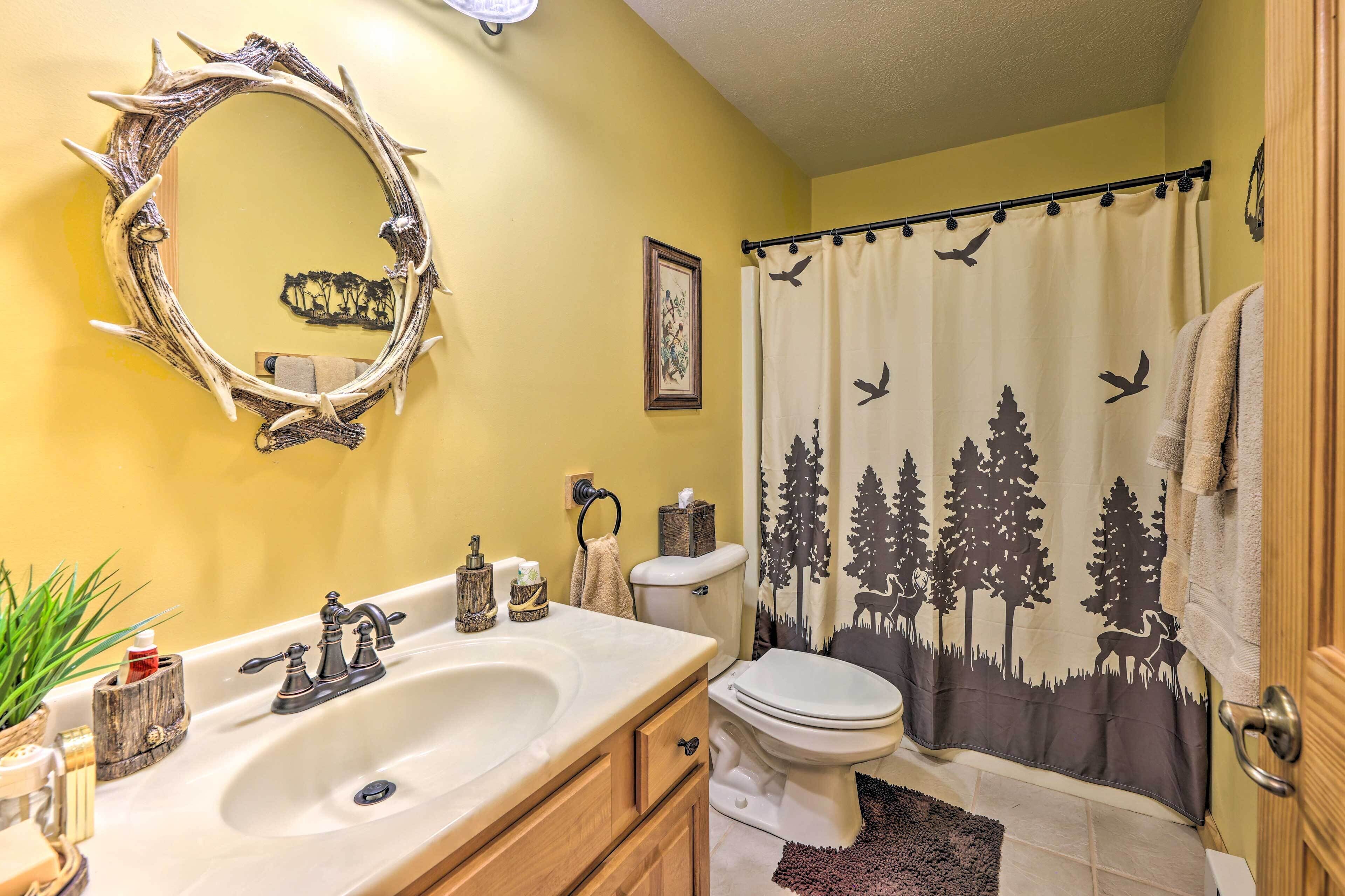 A bathroom with a vanity, sink, mirror, toilet, and shower curtain with a nature theme.