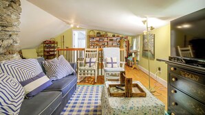 A cozy living room with a stone wall, a sofa, a bookshelf, and a television. - Dainty New Preston Cottage w/ Dock & Lake Views! (New Preston)