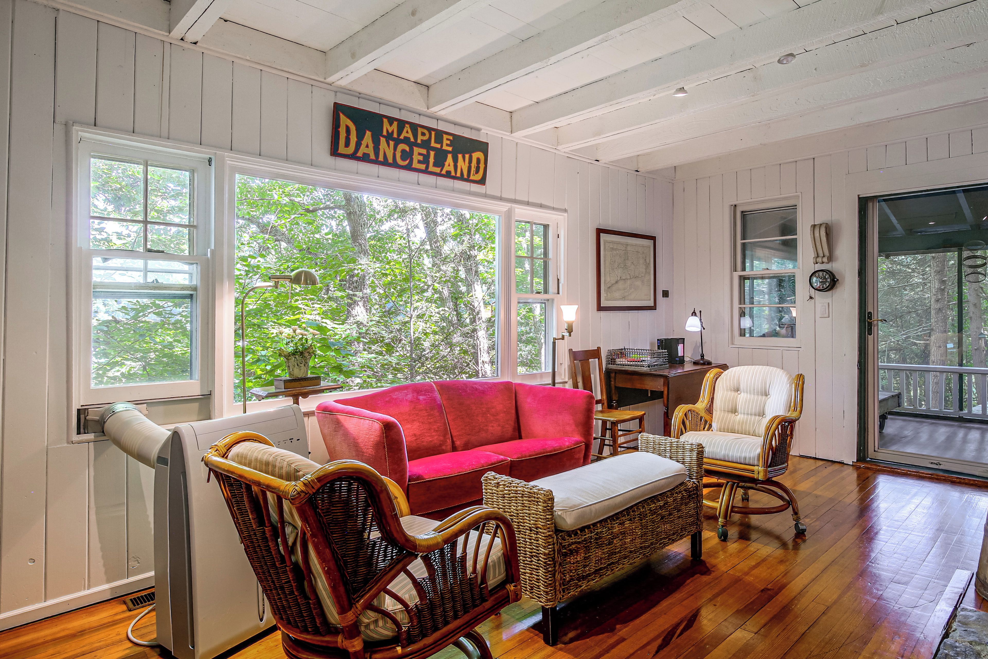 A cozy room with a red sofa, wicker chairs, a desk, and a large window with a view of trees.