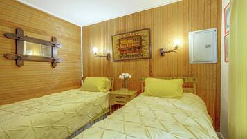 A room with two beds, wooden paneling, a mirror, wall-mounted light fixtures, and a framed picture.