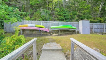A wooden deck with a concrete ramp leading to a fenced area with kayaks.