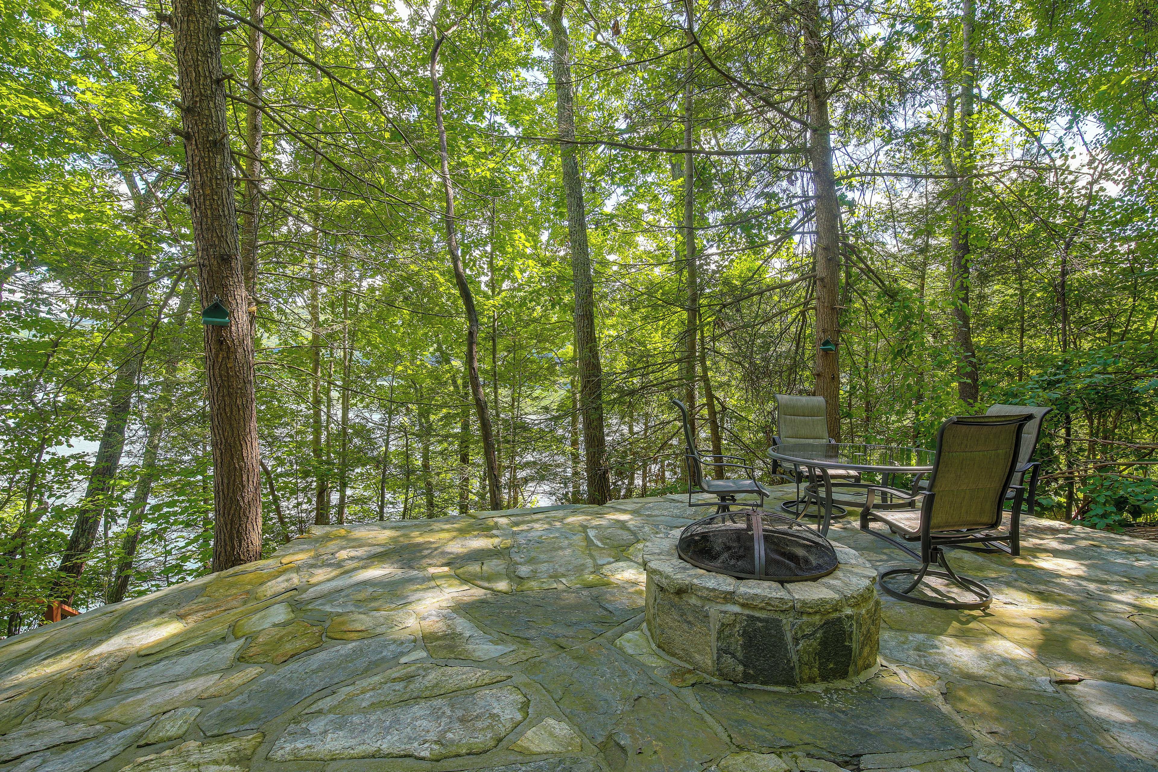 A stone fire pit surrounded by outdoor furniture in a forested area.