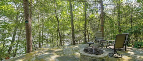 A stone fire pit surrounded by outdoor furniture in a forested area.