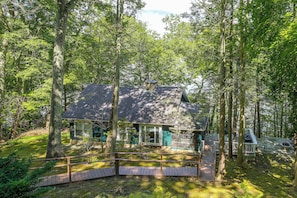 A cabin surrounded by a forest with a wooden deck and a stone fireplace. - Dainty New Preston Cottage w/ Dock & Lake Views! (New Preston)