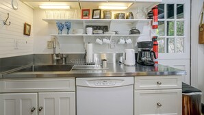 A kitchen with white cabinets, a stainless steel countertop, a coffee maker, and a window with a view of greenery. - Dainty New Preston Cottage w/ Dock & Lake Views! (New Preston)