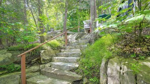 A stone staircase surrounded by lush greenery, leading to a building with a stone wall and a wooden railing. - Dainty New Preston Cottage w/ Dock & Lake Views! (New Preston)