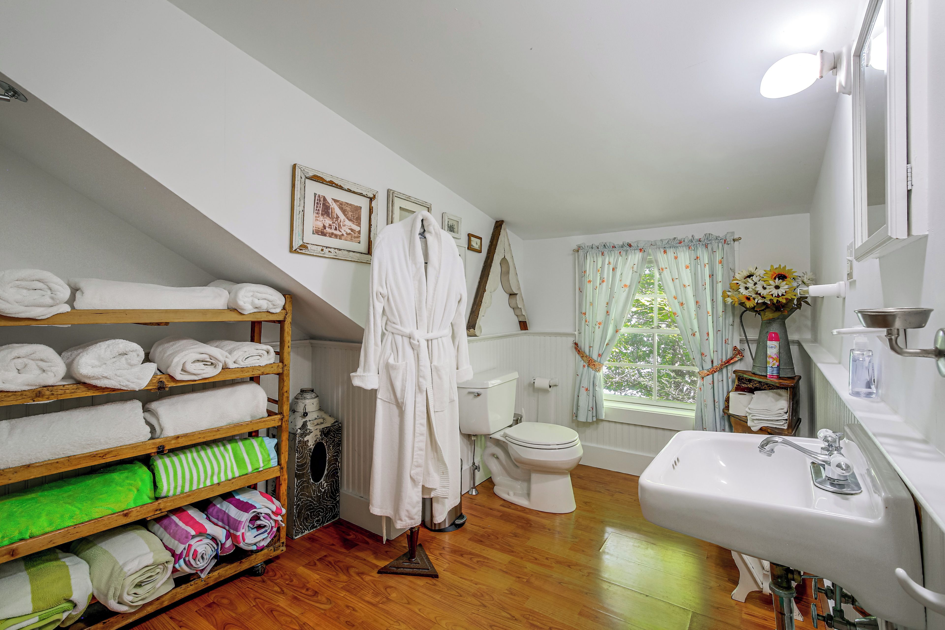A bathroom with a wooden shelf holding towels, a white bathtub, a toilet, and a sink with a mirror.