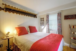 Quarto com cama, luminária de cabeceira, janela com cortinas e prateleira na parede.